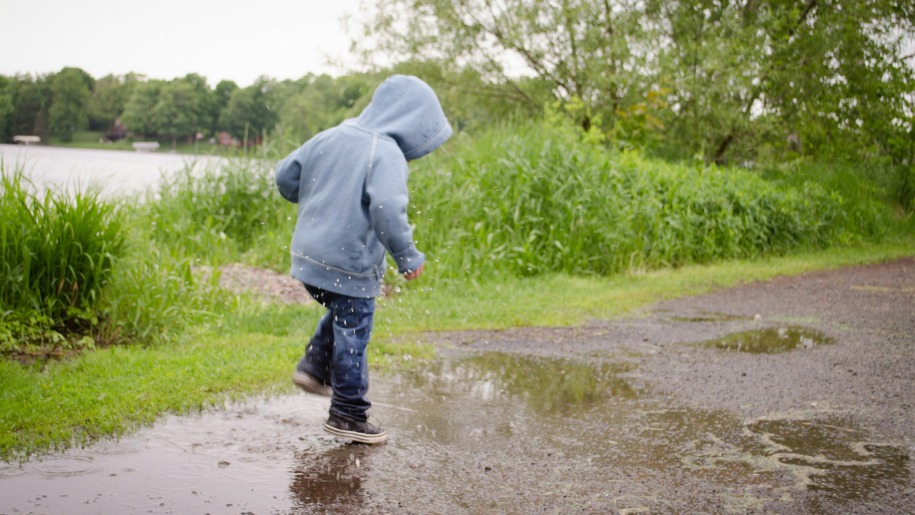 Child splashing in puddles by water.