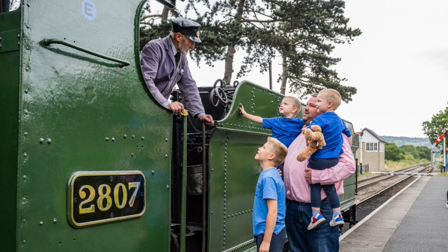Father and three sons talking to the engine driver on a green locomotive.