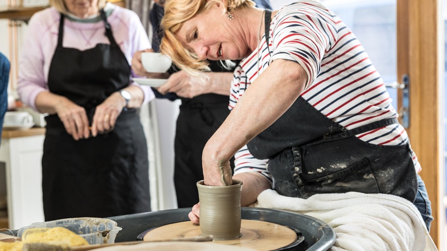 Adult demonstrating how to throw a pot on the potter's wheel at Hot Pot Pottery.