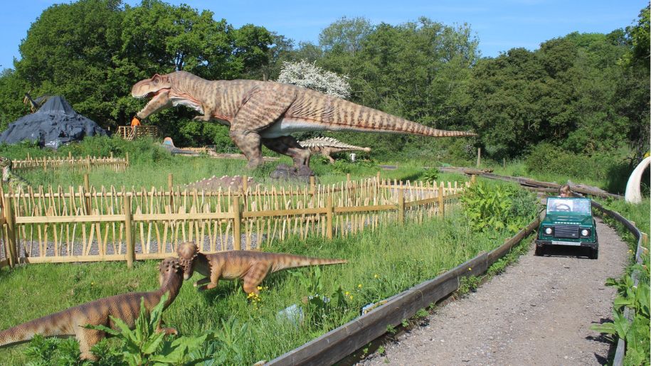 dinosaur model in a field with a drivealong jeep besides it