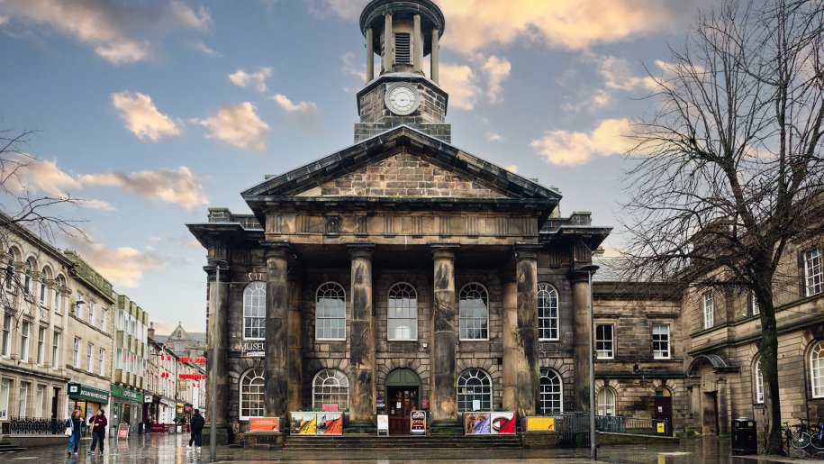 Facade of large stone building with clocktower at sunset.