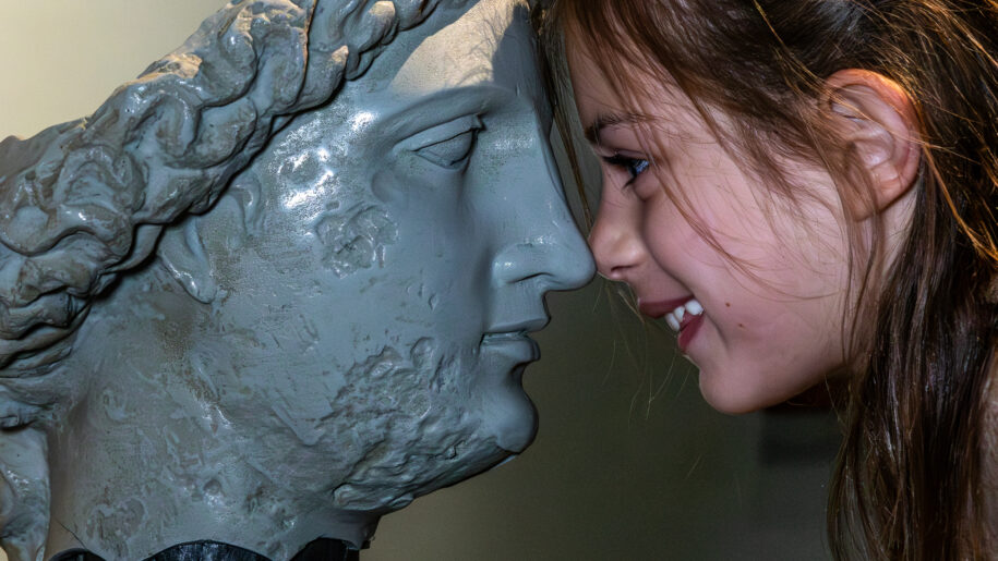 girl puts face to marble statue face