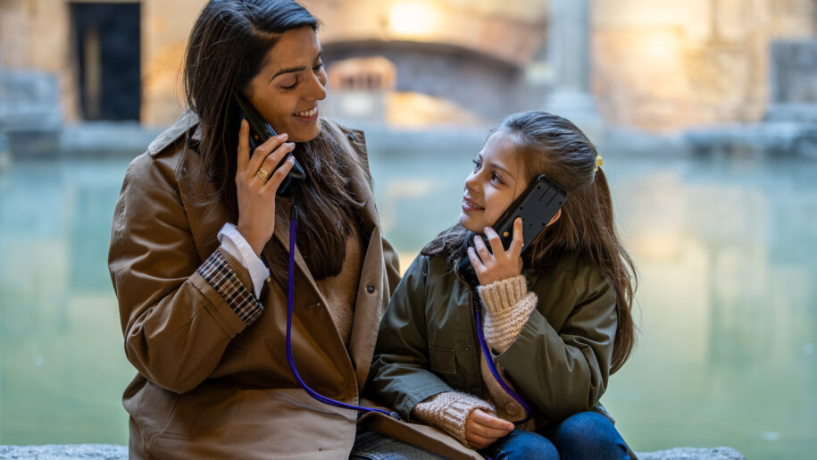 lady and girl listen to handheld tourist guide machines in front of water
