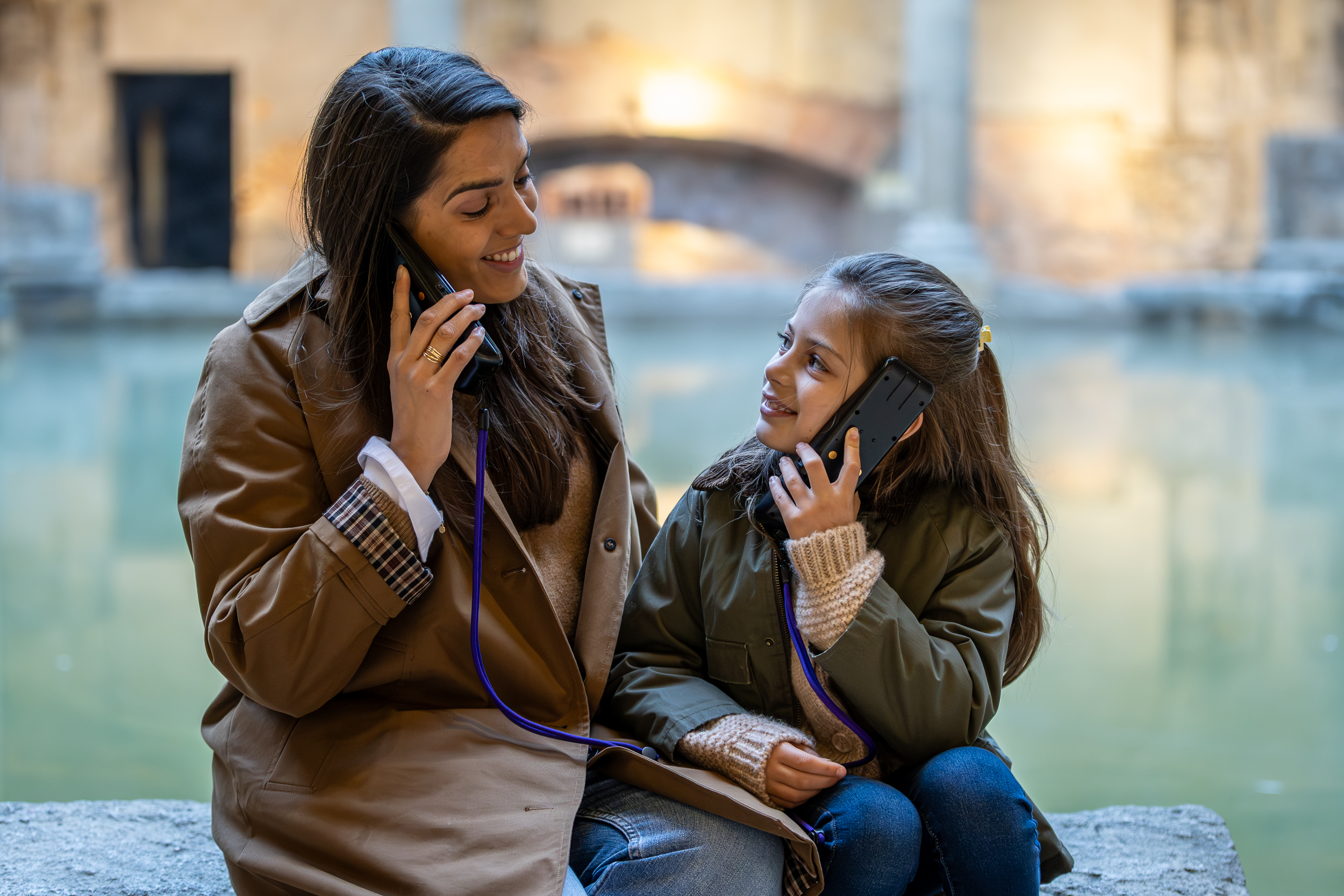 lady and girl listen to handheld tourist guide machines in front of water