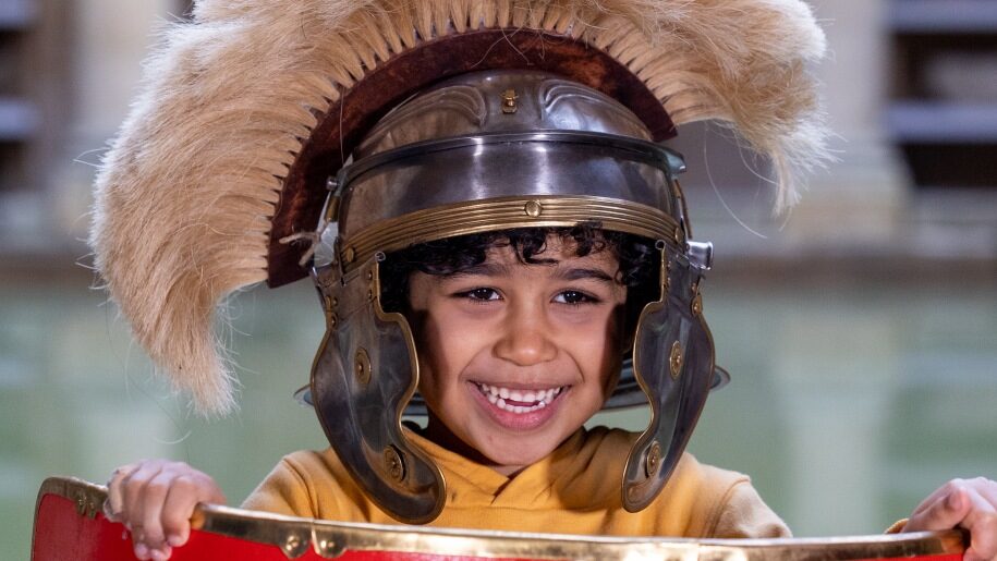 Child holding a shield and wearing a Roman helmet.