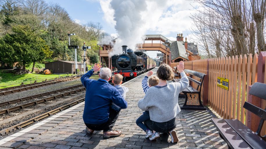 A family waving at a steam train on a platform at the Severn Valley Railway.