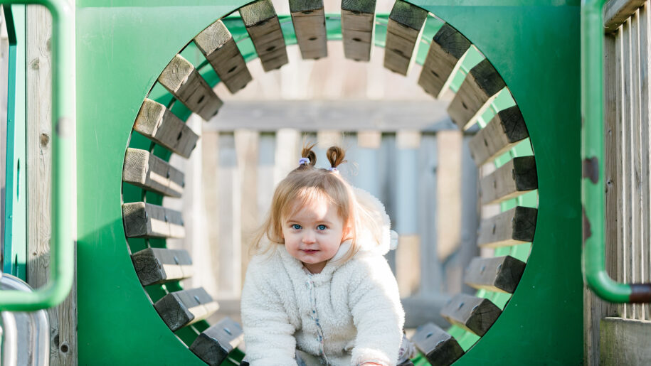 little girl plays in green playground tube