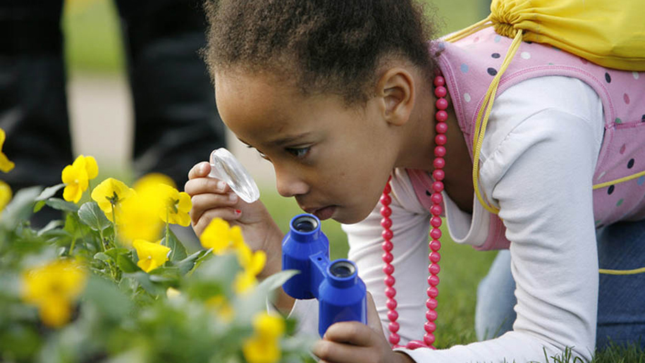 girl inspecting flowers with magnifying glass