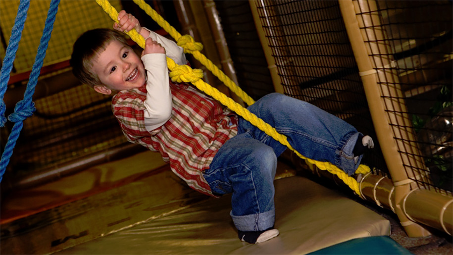boy swinging through ropes in soft play area