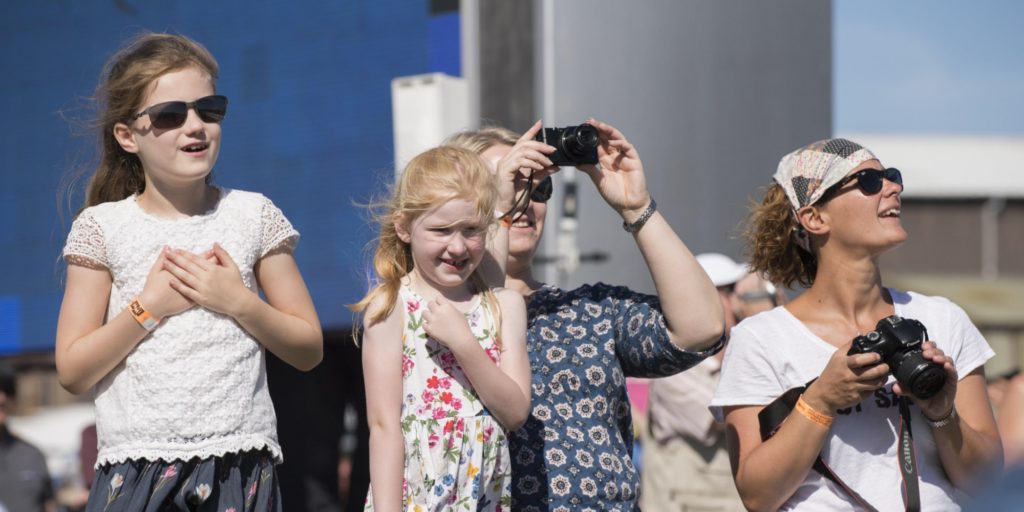 two girls and two women watching planes with cameras in the sunshine