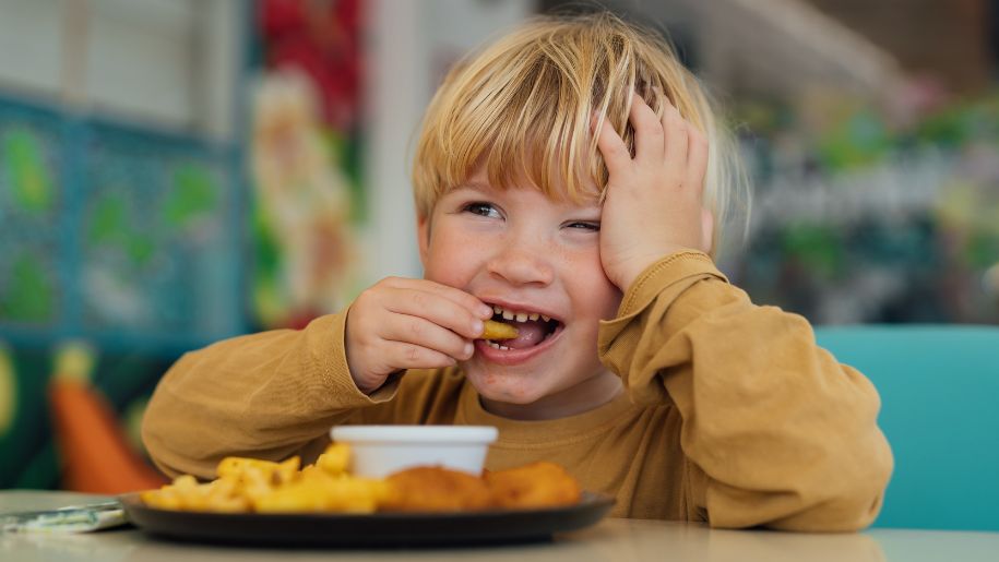 little blonde boy smiling while he eats chips