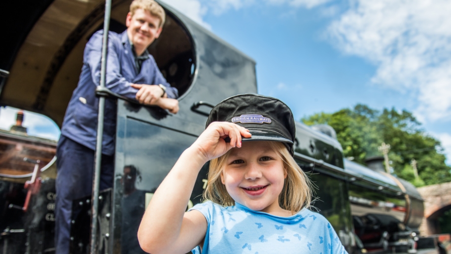 girl with train cap and steam train behind