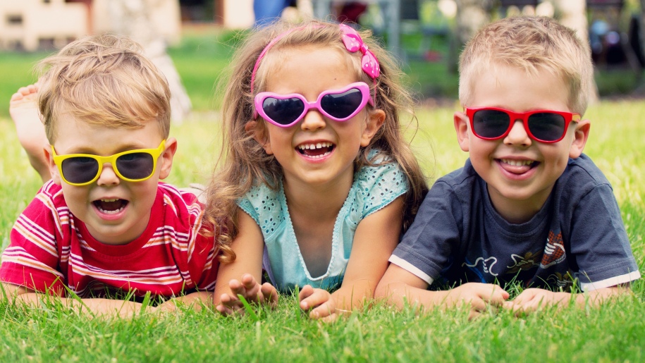 three children wearing sunglasses laying on grass
