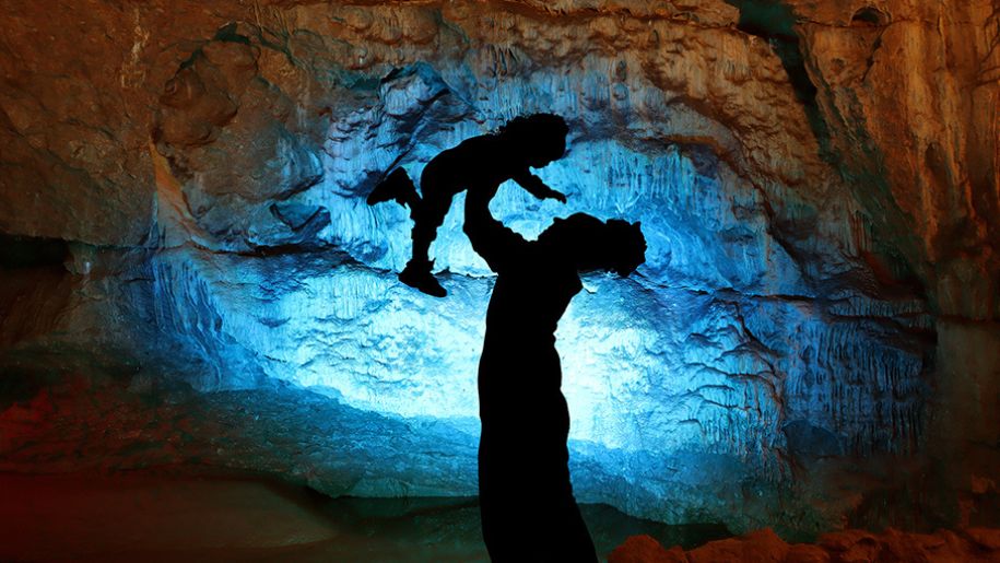 Mother holding son in the air in the shadow of the Wookey Hole caves