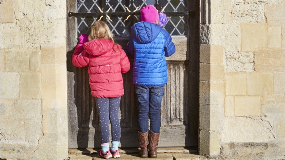 Two girls peering through a door at Anglesey Abbey