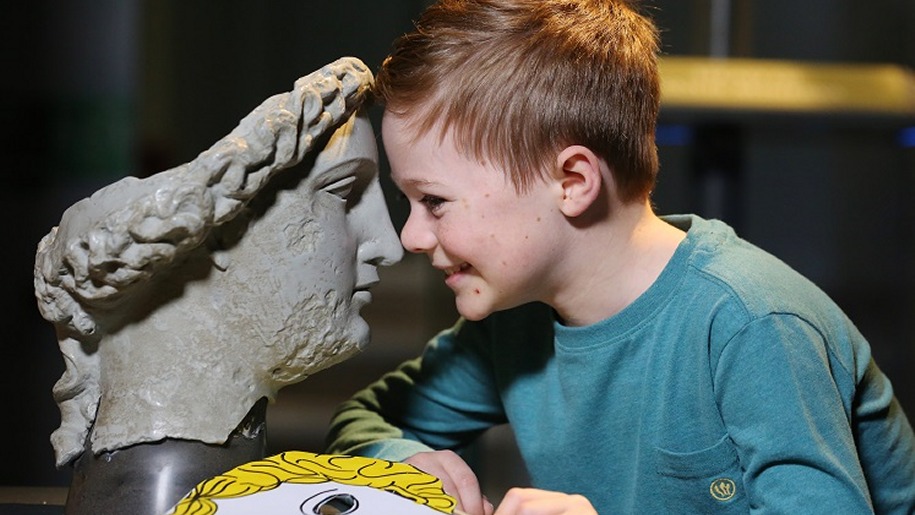 Boy facing Roman mask at Roman Baths