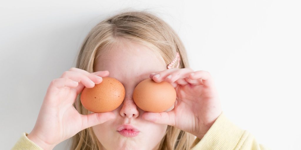 A child holding eggs in front of eyes.