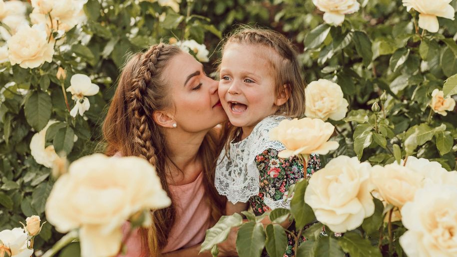 Mother kissing daughter on cheek surrounded by roses