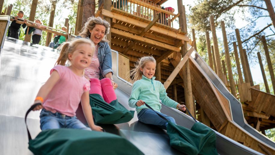 Mother and two girls slifing down large outdoor slide at BeWILDerwood Cheshire
