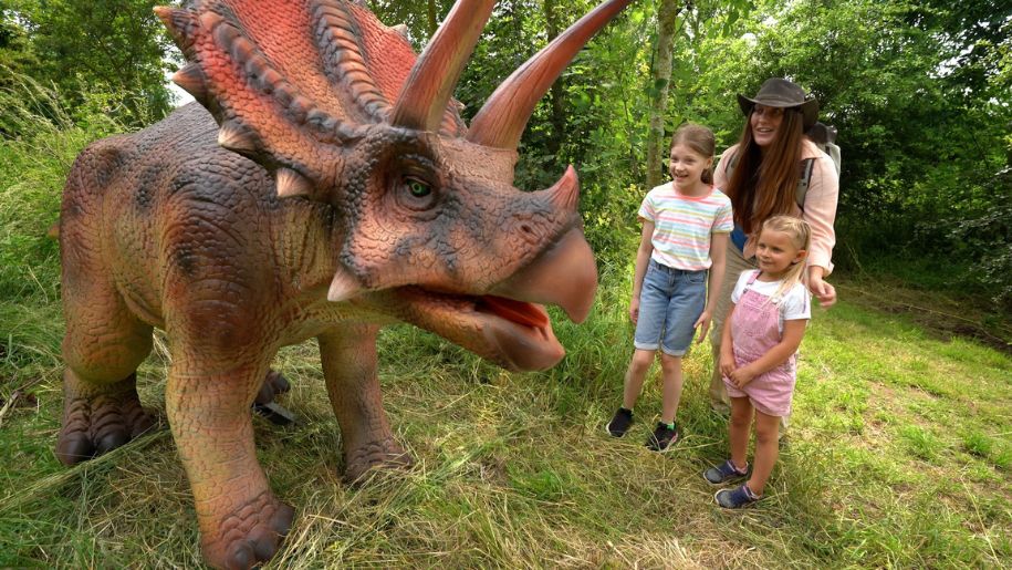 Two children and an explorer looking at dinosaur sculpture 