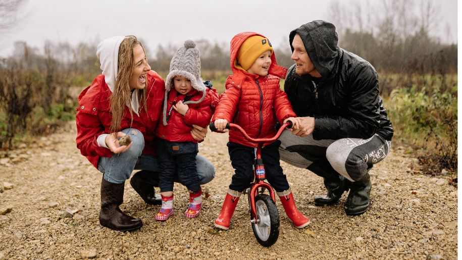 A family walking in the rain with a young child on a bike.
