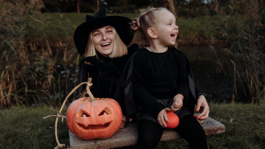 Adult and child in Halloween costumes with a carved pumpkin.
