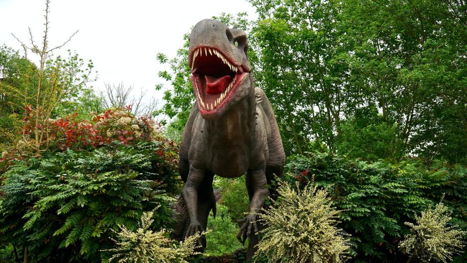Dinosaur standing amongst plants and trees.