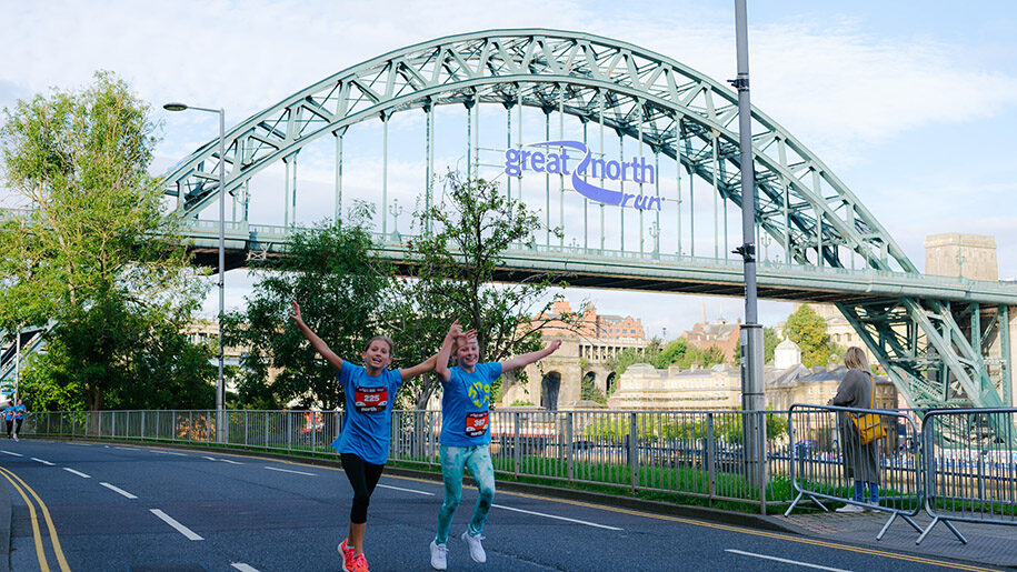 Great North Run boy and girls running under Newcastle bridge with arms in air