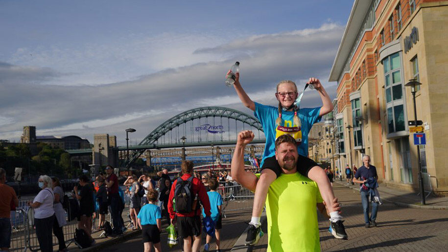 Great North Run girl holding medal sitting on Dad's shoulders