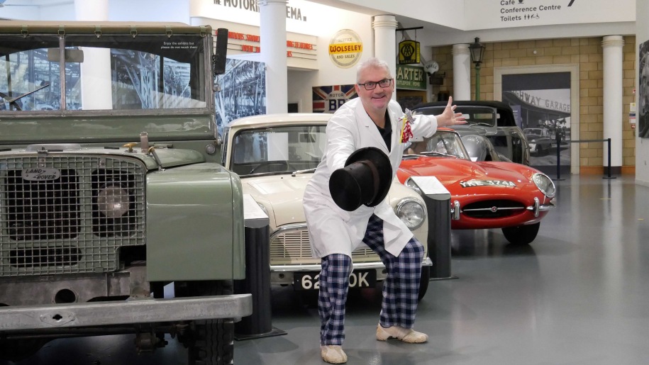 a mad scientist in front of cars at the British Motor Museum