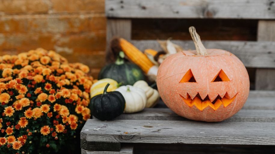 A large orange carved Halloween pumpkin with smaller green and white pumpkins.