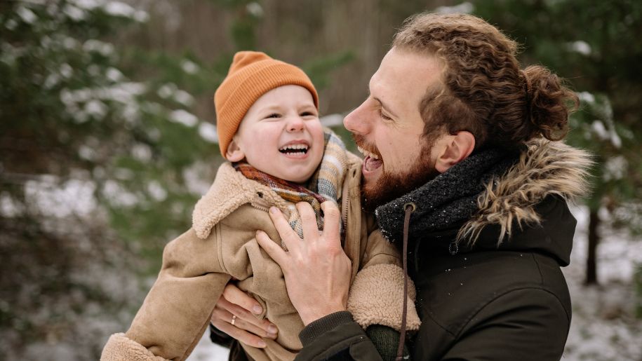 Adult and young child laughing together outside in winter.