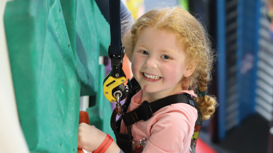 Little girl with plaits wearing harness at climbing wall at Rock Up