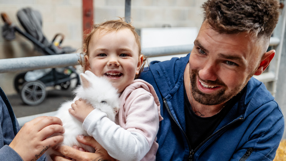 Little girl holding white fluffy rabbit with Dad at Thornton Hall farm
