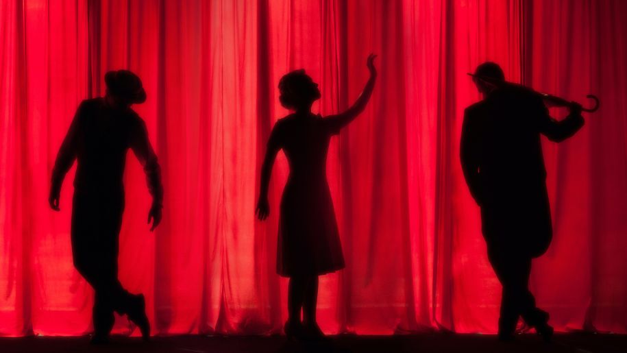 Performers appearing as silhouettes on a theatre stage.