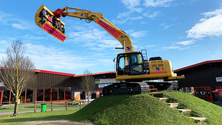 Diggerland digger in front of building with people in bucket.
