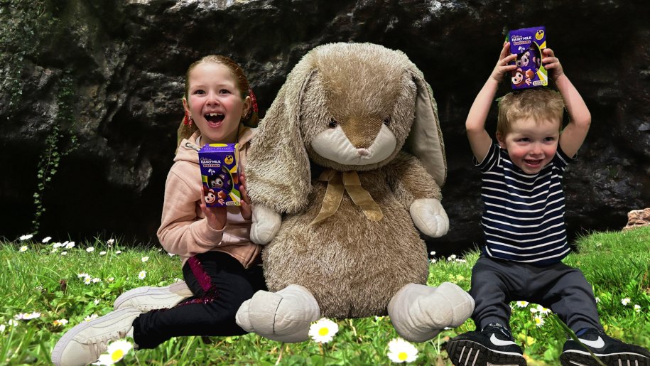 Enormous toy rabbit and two children holding Easter chocolate treats.