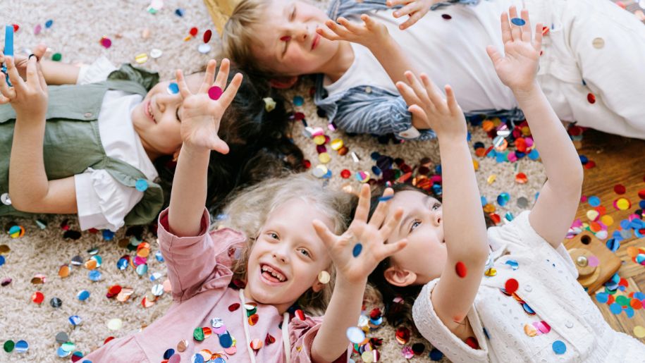 4 children lying on the floor covered in confetti cheering