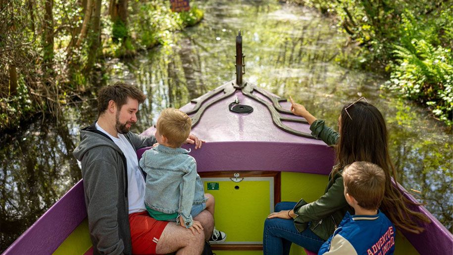 Man and children in a forest-themed boat travelling down a river