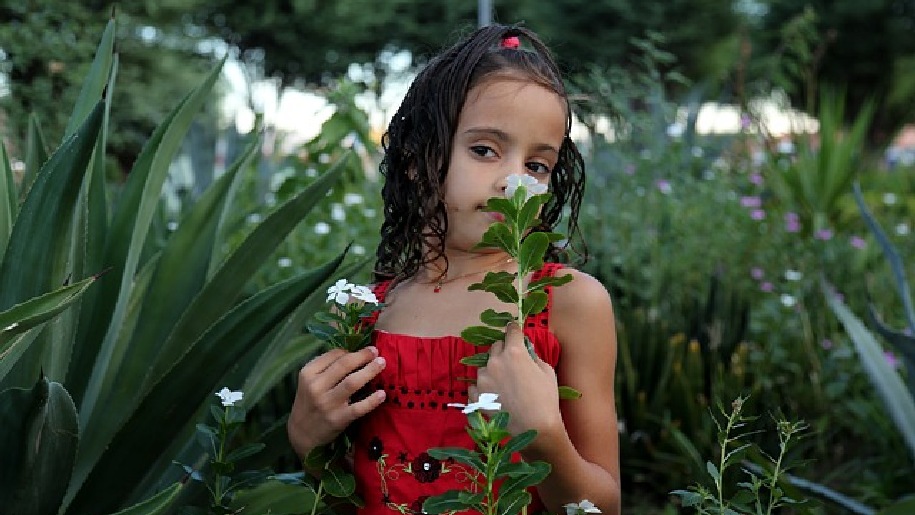 Generic Little girl in a red dress holding and sniffing flowers