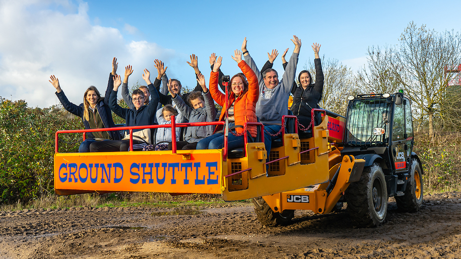 Passengers on ground shuttle tractor at Diggerland with hands in air.