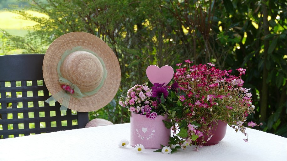 Generic Mother's Day with flowers, a heart and Mum's straw hat at a table in the countryside