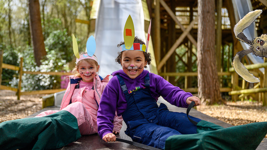 Two children at BeWILDerwood at bottom of slide wearing ears crown