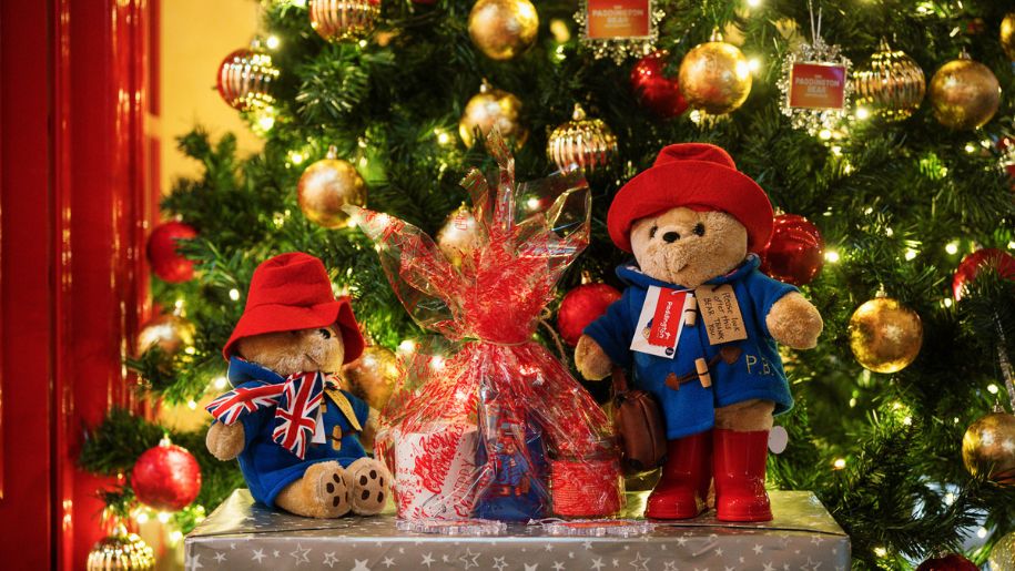 a shot from under a christmas tree, decorated in red and gold baubles, with a bear in a blue coat and red hat underneath