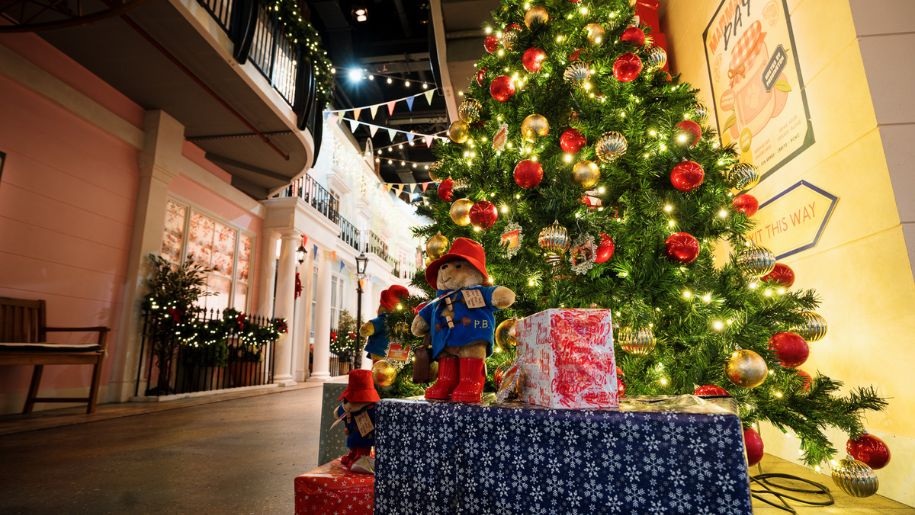a shot from under a christmas tree, decorated in red and gold baubles, with a bear in a blue coat and red hat underneath