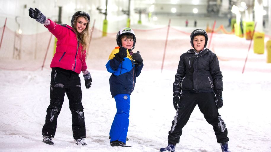 Three young children smiling at the camera on the ski slopes at Snozone