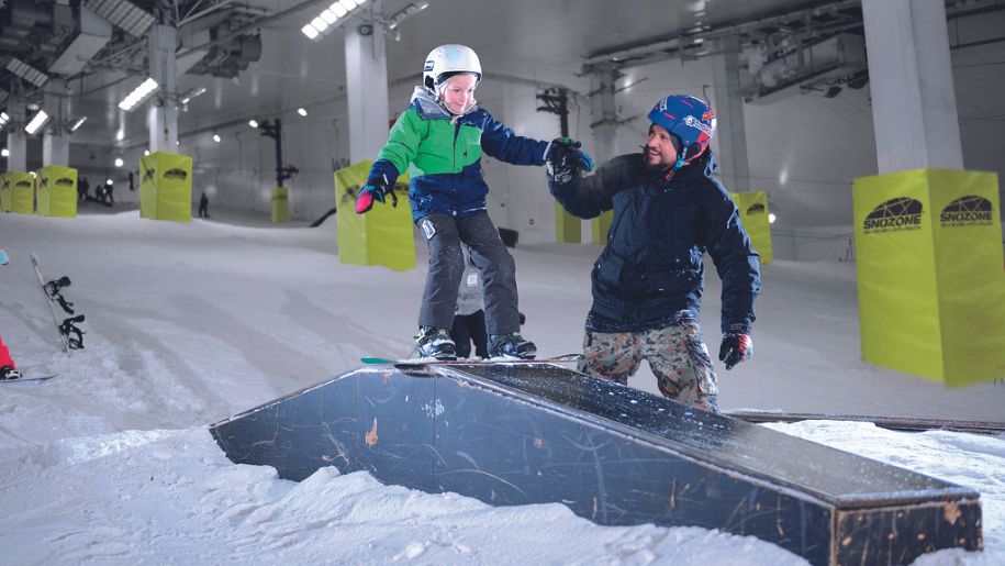 Young child being helped over a ski slope by instructor at Snozone