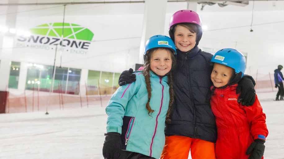3 young children smiling on the ski slopes at Snozone
