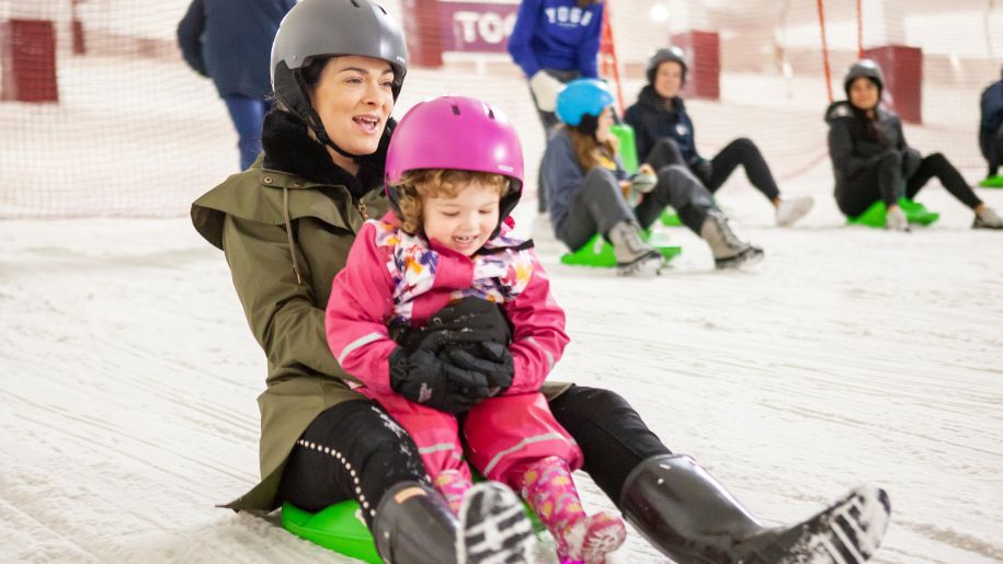 A woman and child sitting on a sled together going down a slope at Snozone