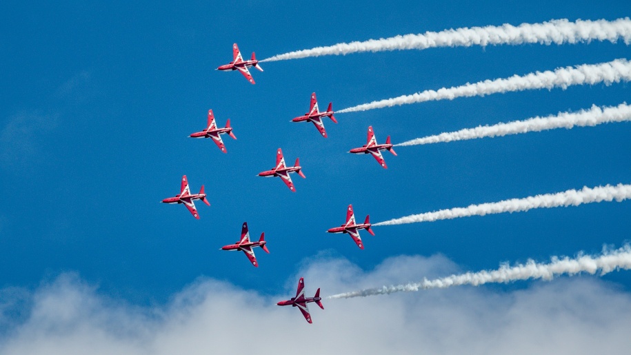 Eight red planes flying across a blue sky.